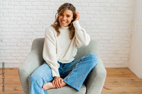 Indooor winter portrait of pretty woman in cozy sweater sittinh on modern sofa at home. photo