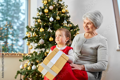 christmas, holidays and family concept - happy grandmother and baby granddaughter with gift box at home