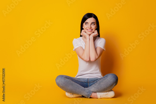 Full body photo of nice cheerful girl sitting on floor dream hands touch chin isolated bright vivid yellow color background