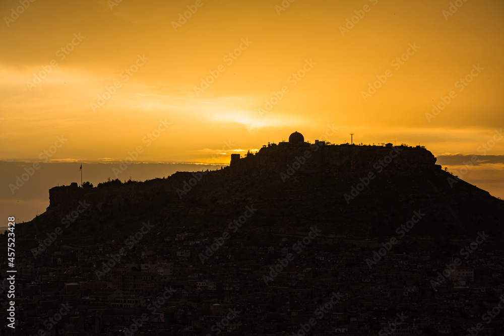 トルコ　マルディンの岩山の山頂に立つマルディン城とサンセットでオレンジ色に染まった空