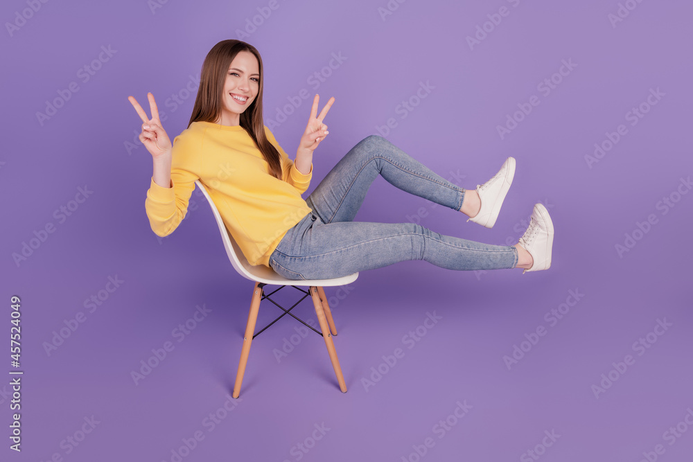 Portrait of friendly carefree sweet lady sit armchair having fun fooling around show v-sign on purple background Portrait of friendly carefree sweet lady sit armchair having fun fooling around show v-sign on purple background