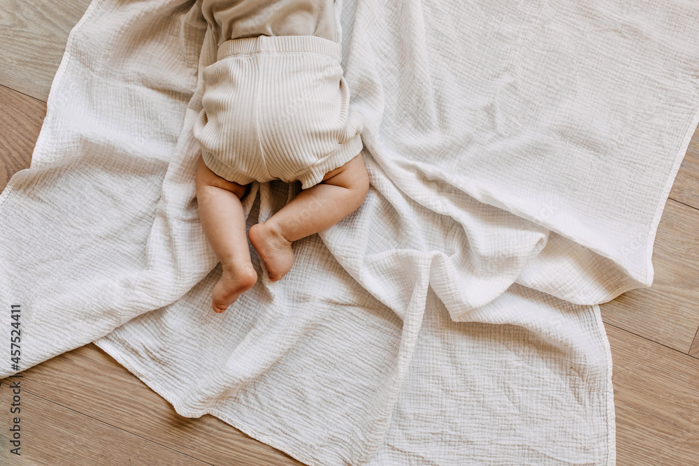 Closeup of barefoot baby lying on tummy on a white muslin blanket on the floor. - obrazy, fototapety, plakaty 