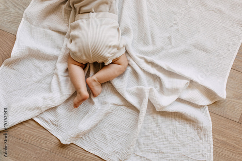 Closeup of barefoot baby lying on tummy on a white muslin blanket on the floor.