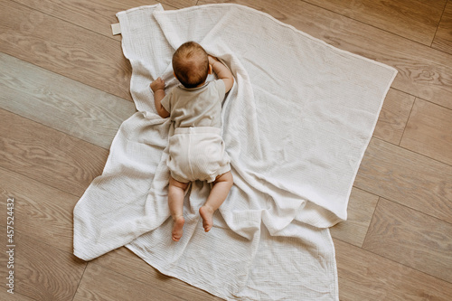 Baby lying on tummy on a white muslin blanket on the floor. Tummy time concept. photo