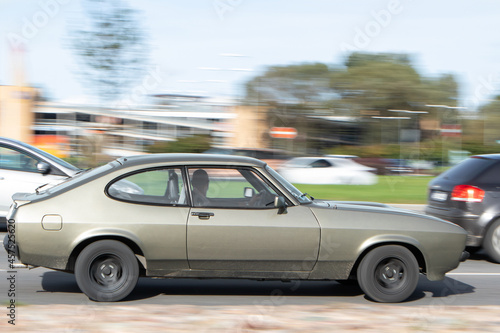 Side view of an old car driving fast down the street. Historic gray-green car. Motion blur