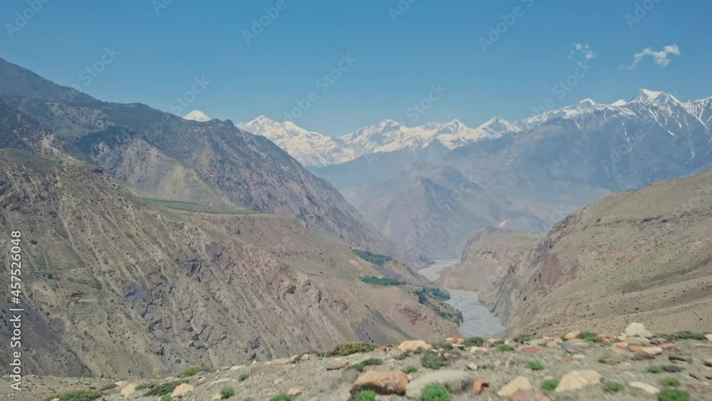 Flight above stone stacks on slope reveal of deep river gorge with snowy mountains in mist