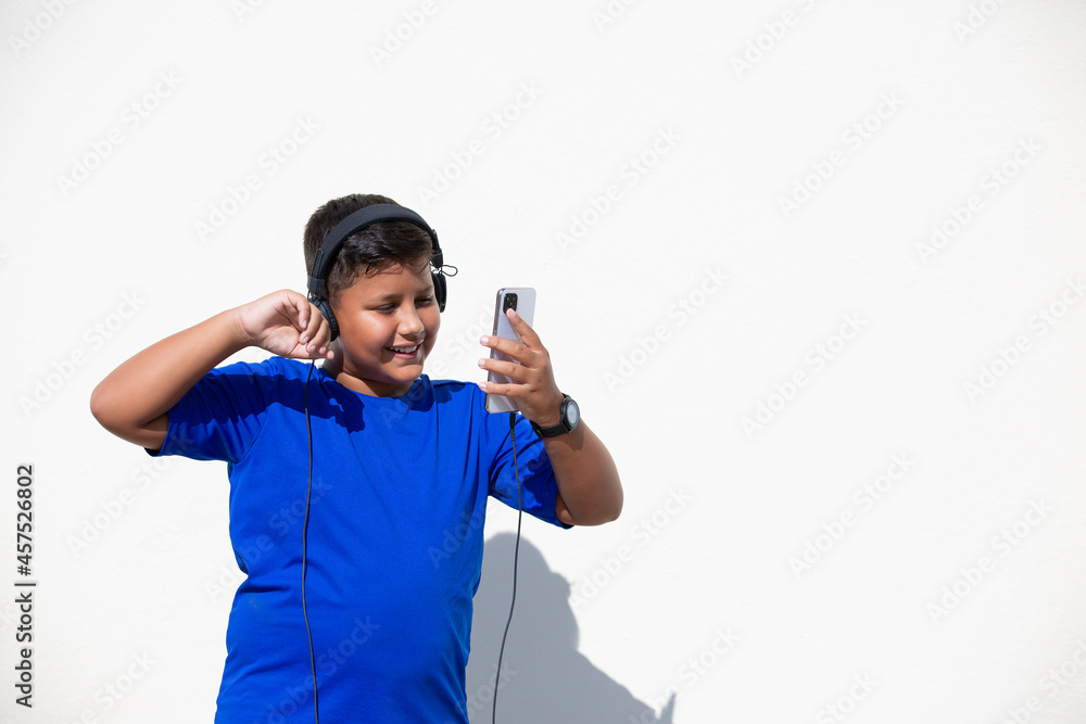 niño sonriente baila y saluda con la mano videollamada con telefono movil y auriculares. aislado fondo amarillo camiseta azul niño sonriente baila y saluda con la mano videollamada con telefono movil y auriculares. aislado fondo amarillo camiseta azul