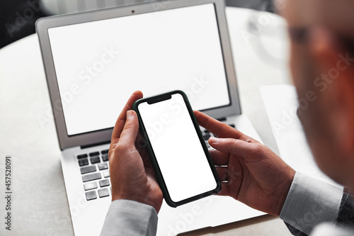 Man holding a mobile phone with a white screen on the background of a laptop with a white screen