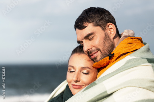 love, relationship and people concept - happy smiling couple in warm blanket on autumn beach