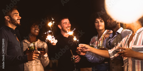 Happy young friends having fun with sparklers fireworks while drinking cocktails on house patio party - Youth people lifestyle and holidays concept