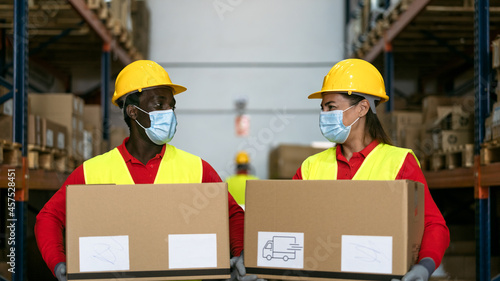 Warehouse workers loading delivery boxes while wearing face mask during corona virus pandemic - Logistic and industry concept
