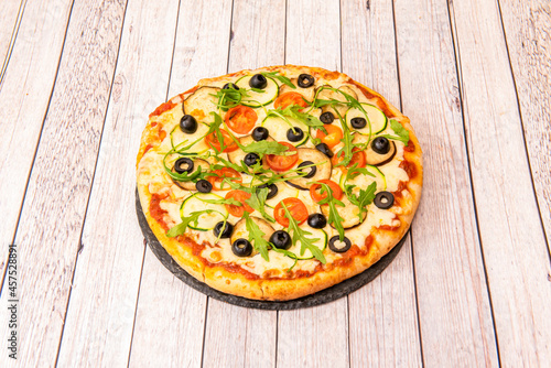 Vegan pizza with potato cheese with arugula, aubergine slices, black olive slices, cherry tomato slices, zucchini slices and tomato