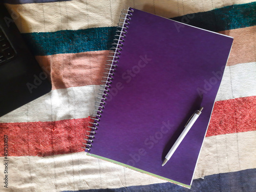empty purple notepad with white pen on it mockup with laptop selective focus