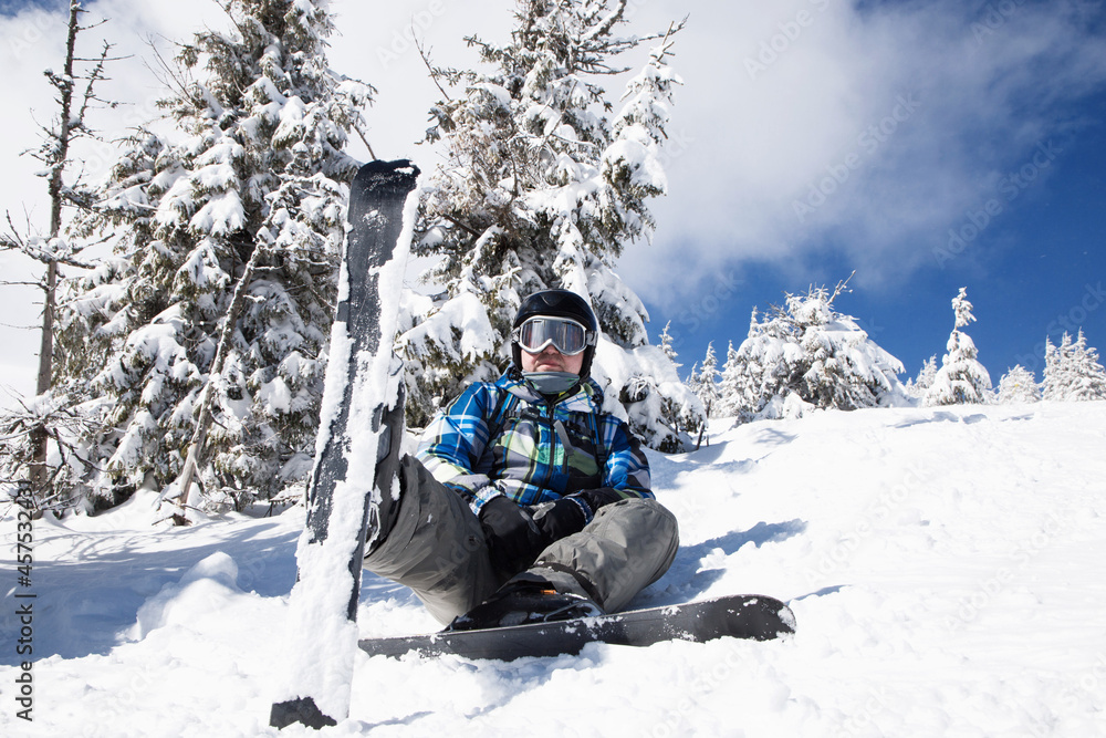 man of about 35-40 years old in winter clothes on skis sits in the snow on a sunny winter day. skier enjoying winter holidays on a snowy slope, relaxation