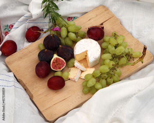 Picnic on the grass. White tablecloth, wooden board with figs, grapes, cheese and plums, bottle of rose wine. Dinner in a garden. 