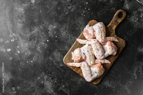 Raw chicken wings on a wooden board on a dark culinary background top view from a copyspace. The process of cooking poultry 