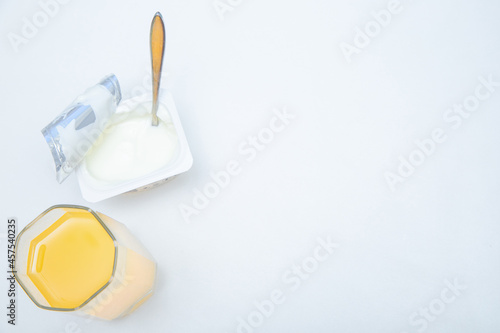 A cup of natural yogurt, a dessert spoon and a glass of orange juice on a white background.