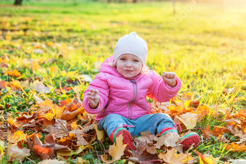 Happy young girl playing under falling yellow leaves in beautiful autumn park on nature walks outdoors. Little child throws up autumn orange maple leaves. Hello autumn concept.