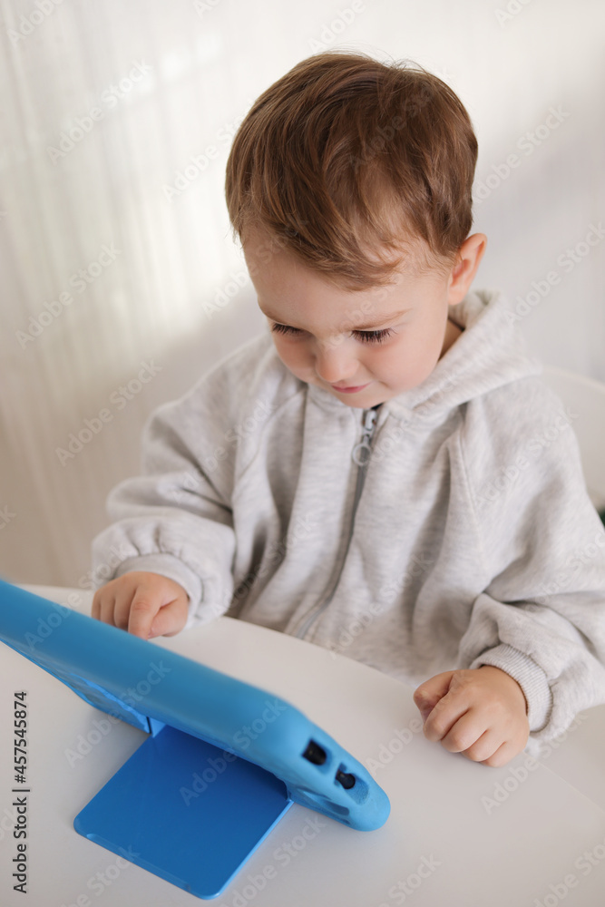Happy little boy playing game on digital tablet at home. Portrait of a child at home watching cartoon on the tablet. Modern kid and education technology. Happy little boy playing game on digital tablet at home. Portrait of a child at home watching cartoon on the tablet. Modern kid and education technology.