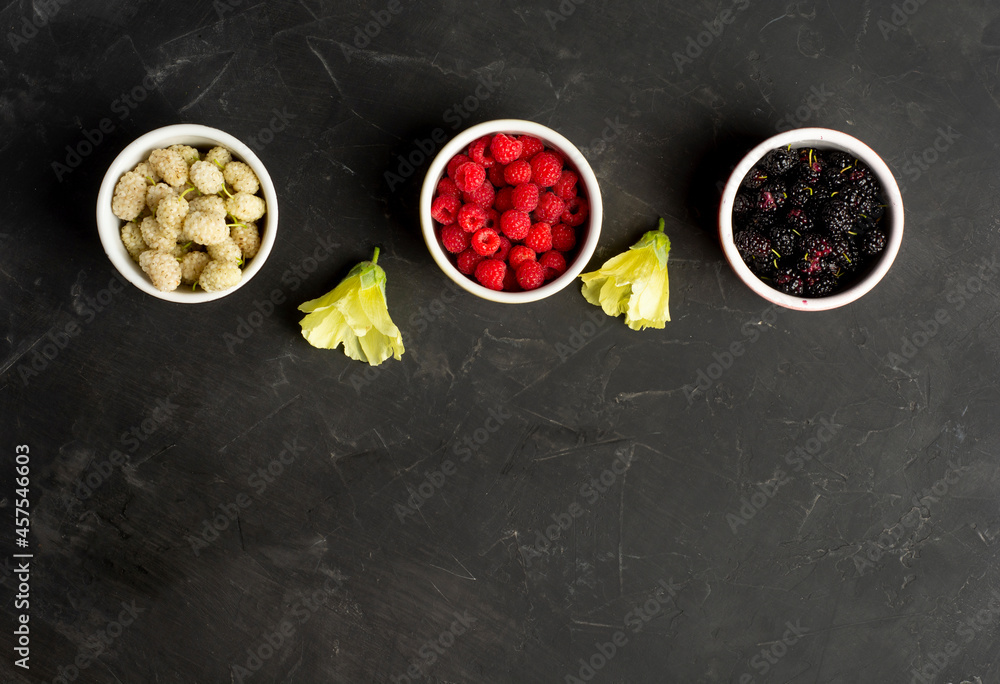 Mix of fresh berries in in bowls on black table . Antioxidants, detox diet, organic fruits. Flat lay with copy space.