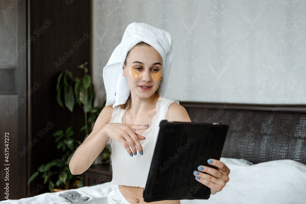 Beauty blogger, vlogger, influencer. Young Woman in pajamas, towel on her head and with cosmetic collagen patches under eyes recording video clip on tablet. Spa, skincare and wellness Beauty blogger, vlogger, influencer. Young Woman in pajamas, towel on her head and with cosmetic collagen patches under eyes recording video clip on tablet. Spa, skincare and wellness