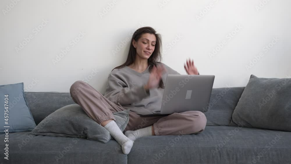 Emotional woman freelancer using device sitting on grey couch, waving hands on a video conference. Gimbal shot of young woman working at home, greet people in online meeting Emotional woman freelancer using device sitting on grey couch, waving hands on a video conference. Gimbal shot of young woman working at home, greet people in online meeting