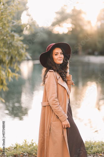 A pretty single woman in an elegant hat and stylish outerwear walks in an fall park among the trees enjoys solitude in nature in autumn outdoor, selective focus © Елизавета Старкова