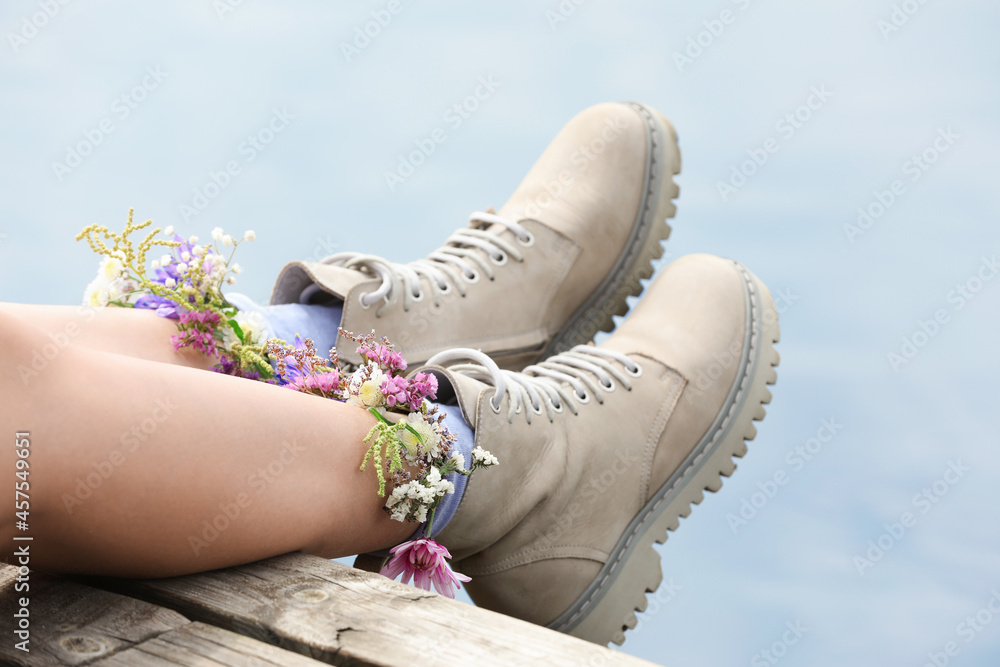 Naklejka premium Woman sitting on wooden pier with flowers in socks outdoors, closeup