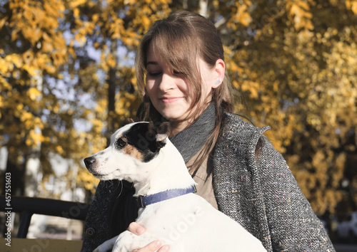 young woman holding jack russel terrier dog while it liiking aside. happy dog with owner outdoors. autumn evening in the park. photo