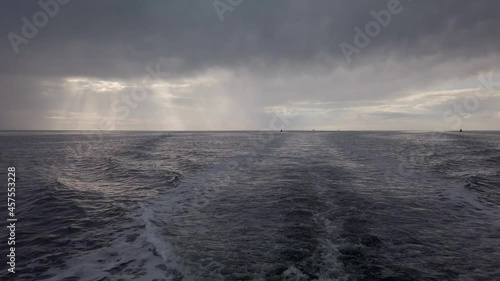 Tilt up from Wake onto Open North Sea with Dramatic Sky after a Rain Storm. Dark Clouds and Rays of Sunshine. Filmed from the back of a boat. photo