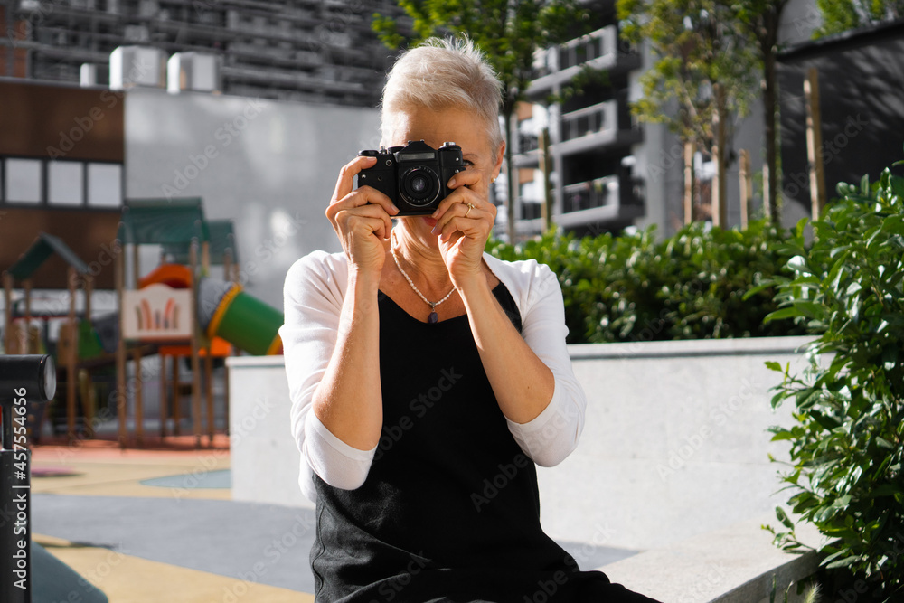A beautiful senior woman sits in a park and takes photos with a photo camera. A beautiful senior woman sits in a park and takes photos with a photo camera.