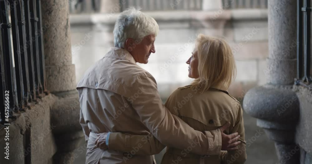 Back view of stylish senior couple hugging standing near city river Back view of stylish senior couple hugging standing near city river