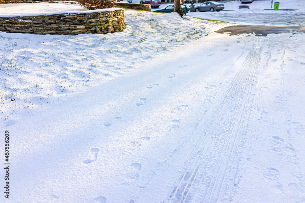 Blue driveway of house in neighborhood with snow covered ground from white storm in Virginia suburbs with footprints and car tracks on road street shining from sunlight Blue driveway of house in neighborhood with snow covered ground from white storm in Virginia suburbs with footprints and car tracks on road street shining from sunlight