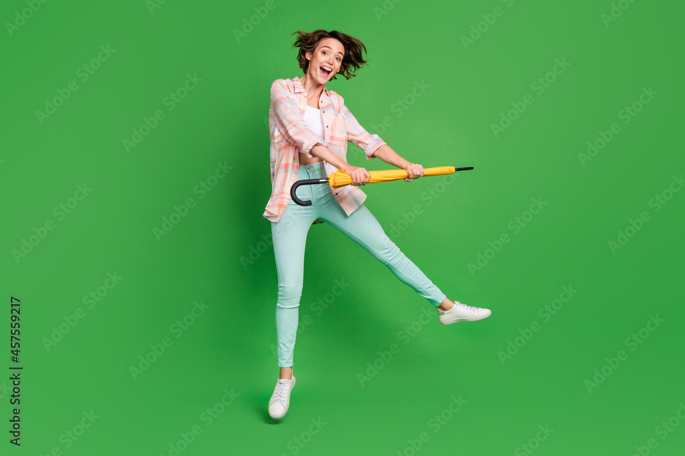 Full length photo of excited cheerful happy woman jump up hold umbrella forecast isolated on green color background Full length photo of excited cheerful happy woman jump up hold umbrella forecast isolated on green color background