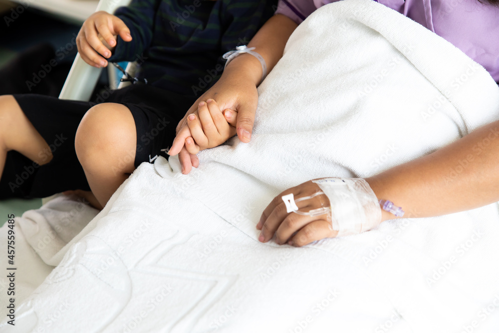 Son holding hand mother give encouragement. Asian mother lies on hospital patient bed with her cute little son at hospital room.