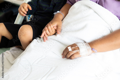 Son holding hand mother give encouragement. Asian mother lies on hospital patient bed with her cute little son at hospital room.