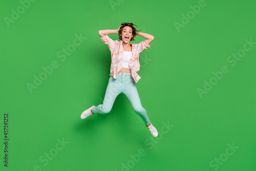 Full size photo of young woman amazed shocked sale jump up hold hand head isolated on green color background