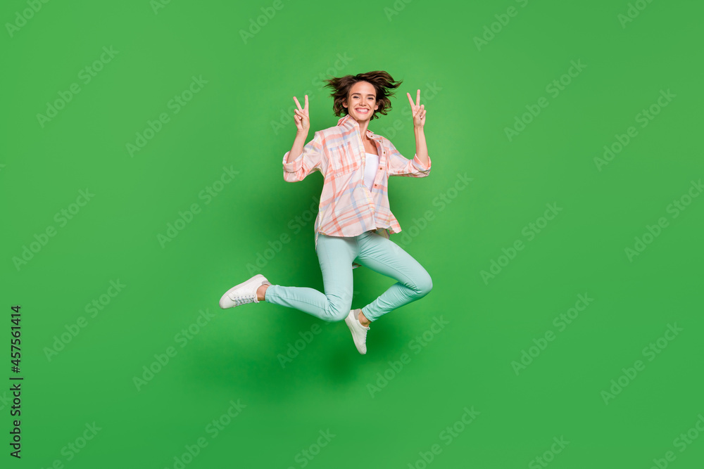 Full size photo of cheerful happy young woman jump up make fingers v-signs cool isolated on green color background Full size photo of cheerful happy young woman jump up make fingers v-signs cool isolated on green color background