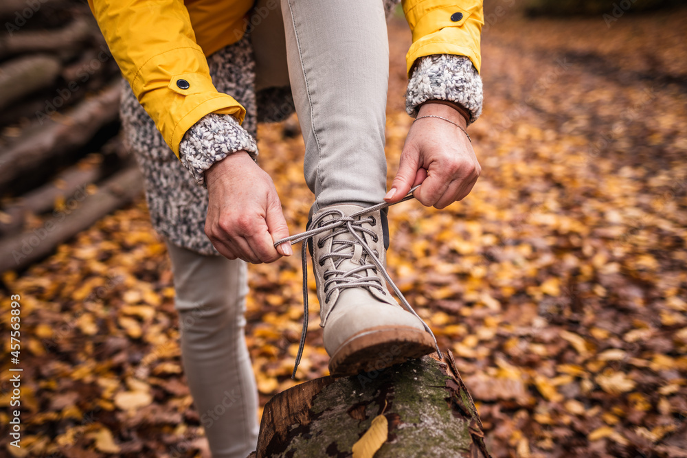 Woman tying shoelace on her hiking boot. Tourist is getting ready for autumn hike at forest trekking trail - obrazy, fototapety, plakaty 