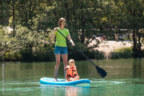 Young smiling woman paddling on a SUP - stand up paddle board, while her daughter sitting on it photo