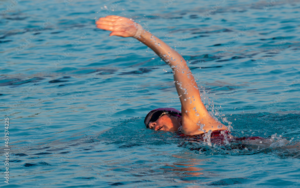 Female freestyle swimming in a pool with the sun lighting up her face