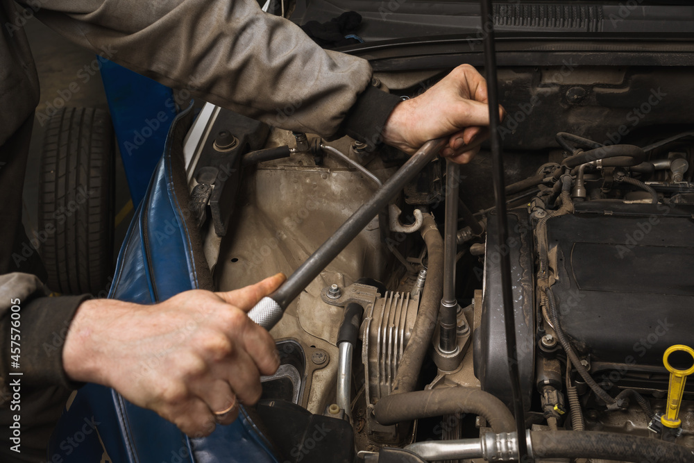 An auto mechanic unscrews the engine mount to replace the timing belt An auto mechanic unscrews the engine mount to replace the timing belt