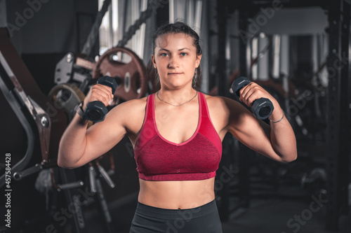 Young woman with dumbbells in the gym. Portrait of young attractive woman in sport clothes holding weight dumbbell doing fitness workout © andyborodaty