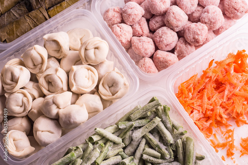 Frozen vegetables and semi-finished meat products in plastic containers on a white plate. meatballs, dumplings, chopped beans and grated carrots