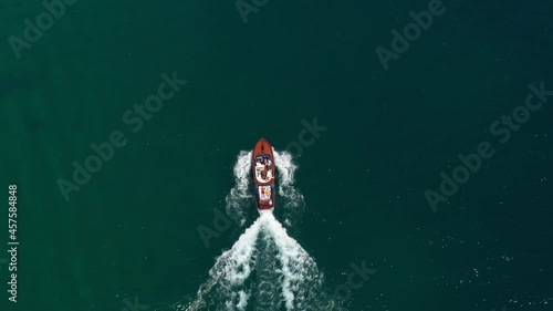 Wooden runabout movement on water. Wooden boat top view moves at speed in the reflection of the sun. Drone view of a Boat with people the blue clear waters.Classic Italian motor boat.