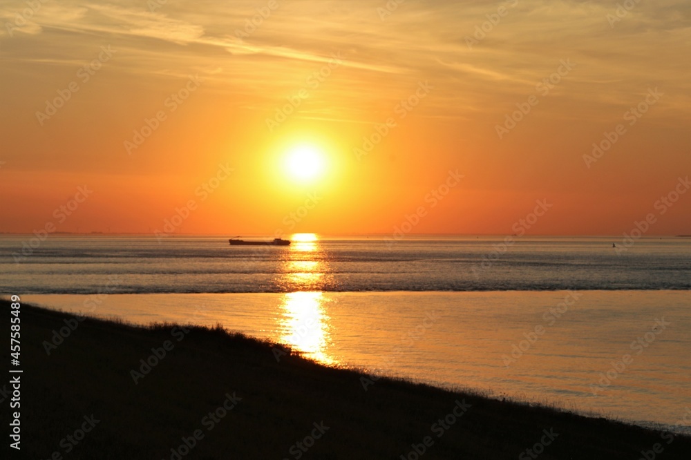 an orange seascape at the dutch coast in zeeland during sunset with a ship and waves in the water 