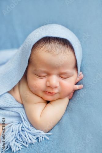 Sleeping newborn baby on a blue background covered by blanket. A few days from birth. Hands under the cheek.