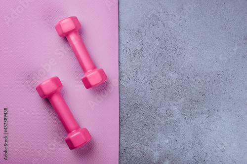 Top view of sport mat and pink dumbbells on marble grey background or set for pilates or fitness practice with copy space.