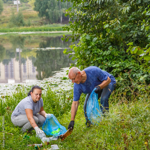A woman and a man volunteers removes garbage from a green area dump.