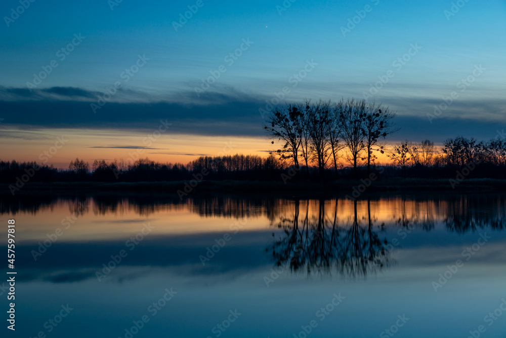 Reflection of trees in the water after sunset